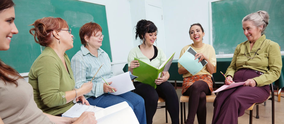 Weibliche Kursteilnehmer sitzen im Stuhlkreis in einem Klassenzimmer und unterhalten sich.