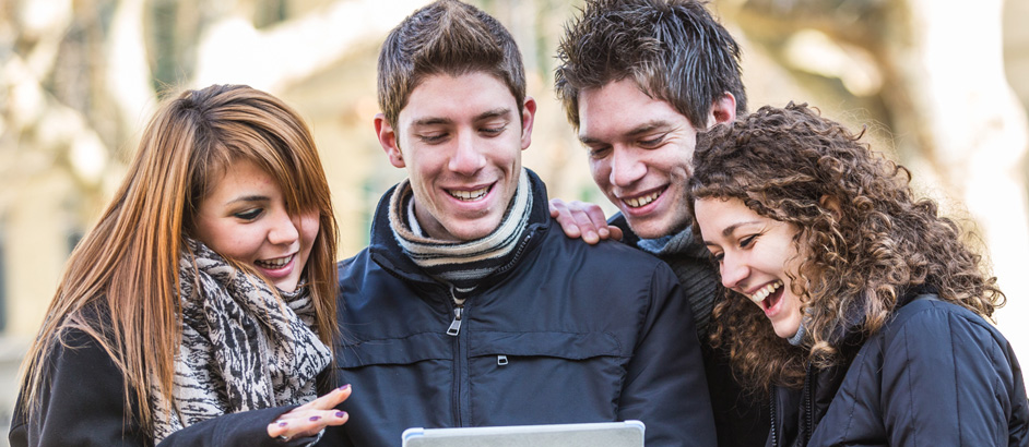 Vier jugendliche Freunde schauen auf ein Tablet und lachen.