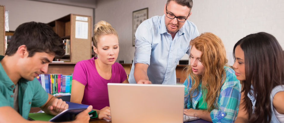 Ein Lehrer erklärt Schülerinnen etwas am Laptop.