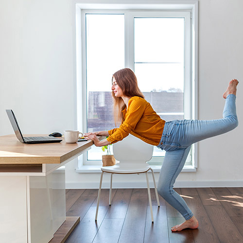 Eine junge Frau macht am Tisch vor einem Laptop Gymnastik.