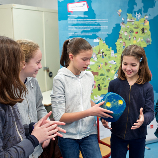 Schülerinnen stehen im Klassenzimmer und spielen mit einem großen Würfel.