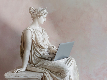 Eine römische Frauenstatue aus Marmor sitzt auf einem Marmorblock. Auf ihrem Schoß liegt ein silberfarbener Laptop.