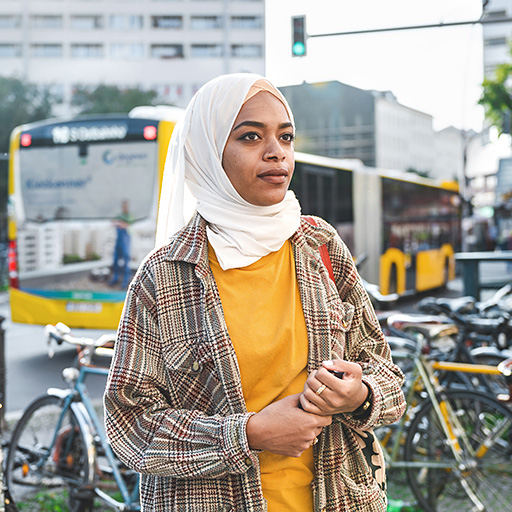 Frau mit Kopftuch steht vor einem Bus und Fahrrädern in einer deutschen Stadt.