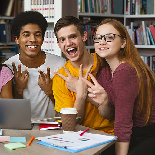 Gruppe von Studenten sitzen in der Bibliothek und zeigen Victory-Zeichen